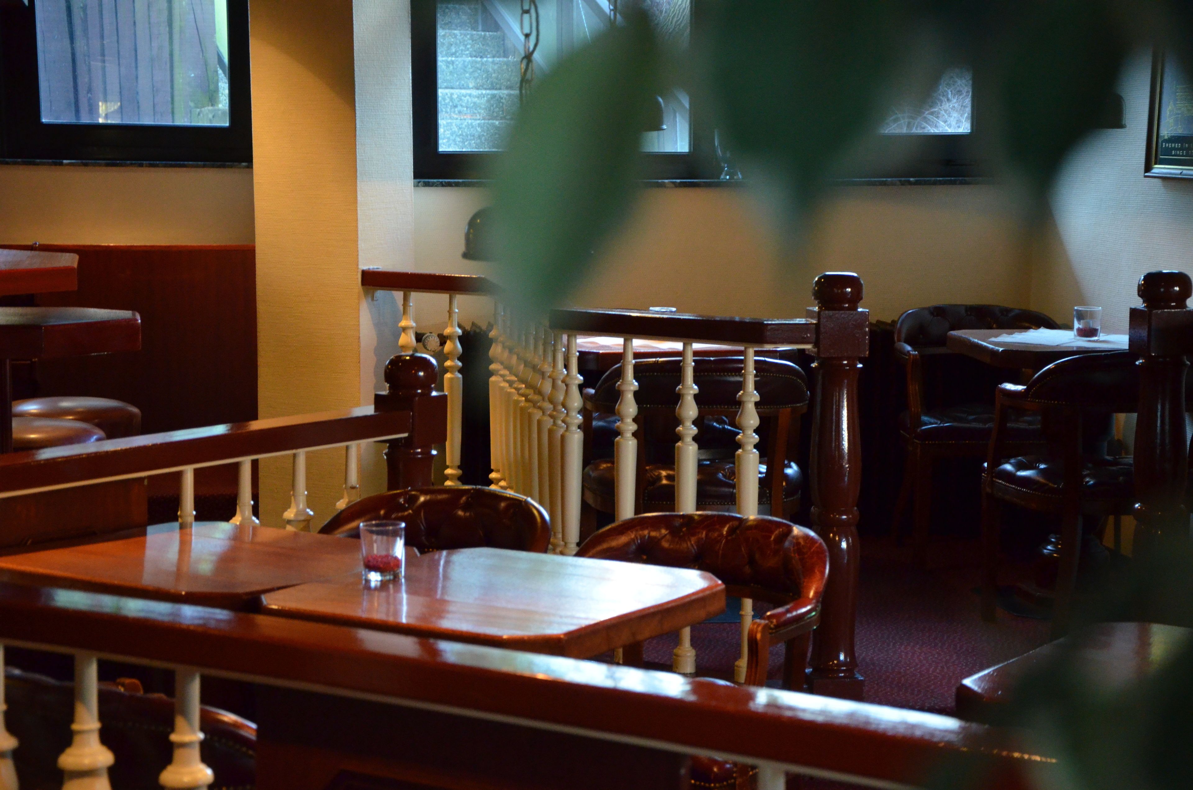 Un interior de restaurante con mesas y sillas de madera, una escalera con barandilla blanca y un ventanal con vista a árboles.