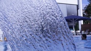 A swimming pool with a waterfall feature, lounge chairs, and a covered area with umbrellas. - Karaman Group Hotel (Bad Nenndorf)