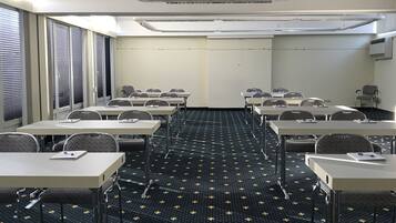 A conference room with tables and chairs, a patterned carpet, and a plain wall with an air conditioning unit.