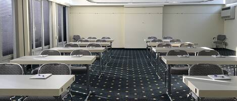 Una sala de conferencias con mesas y sillas, una alfombra estampada y una pared lisa con un equipo de aire acondicionado.
