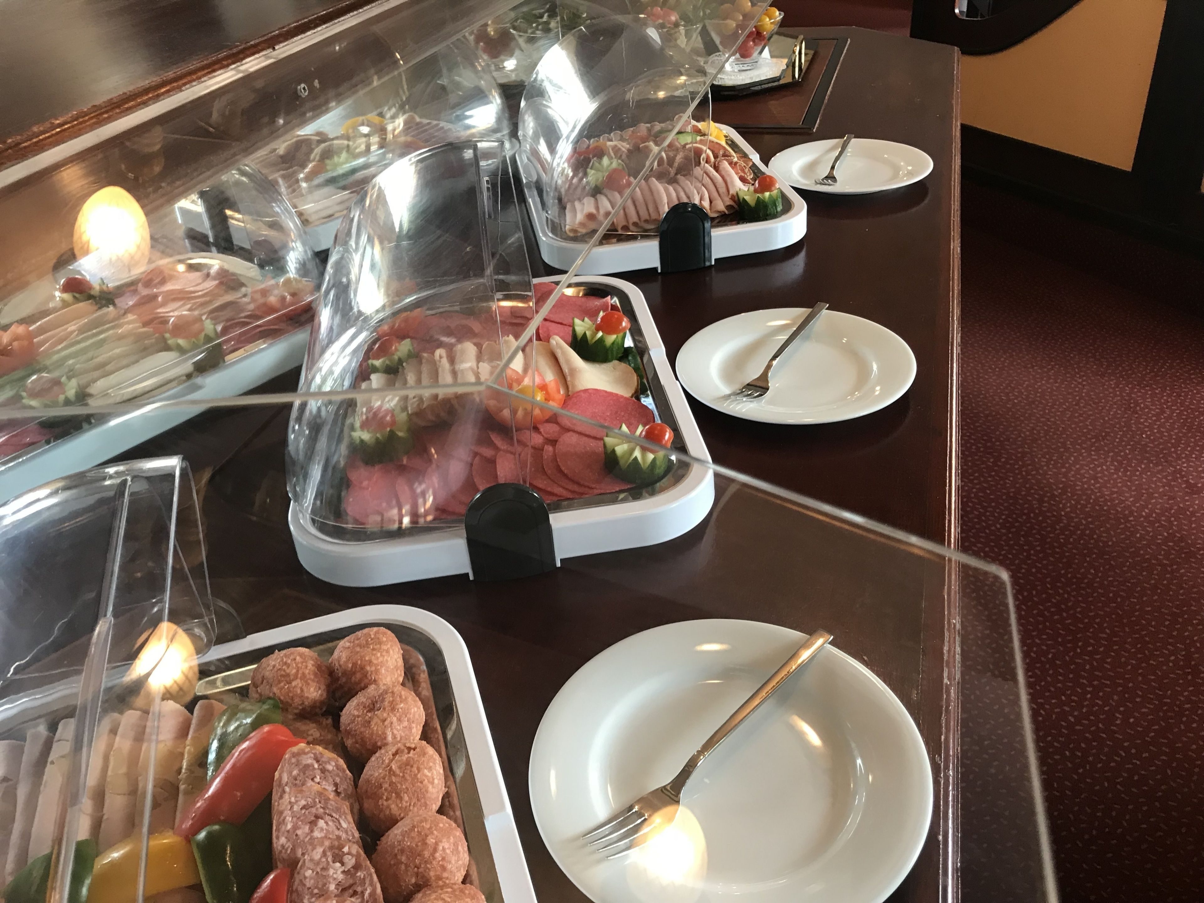Una mesa de buffet con diversos alimentos, como carnes, verduras y panecillos, cubiertos con plástico transparente.