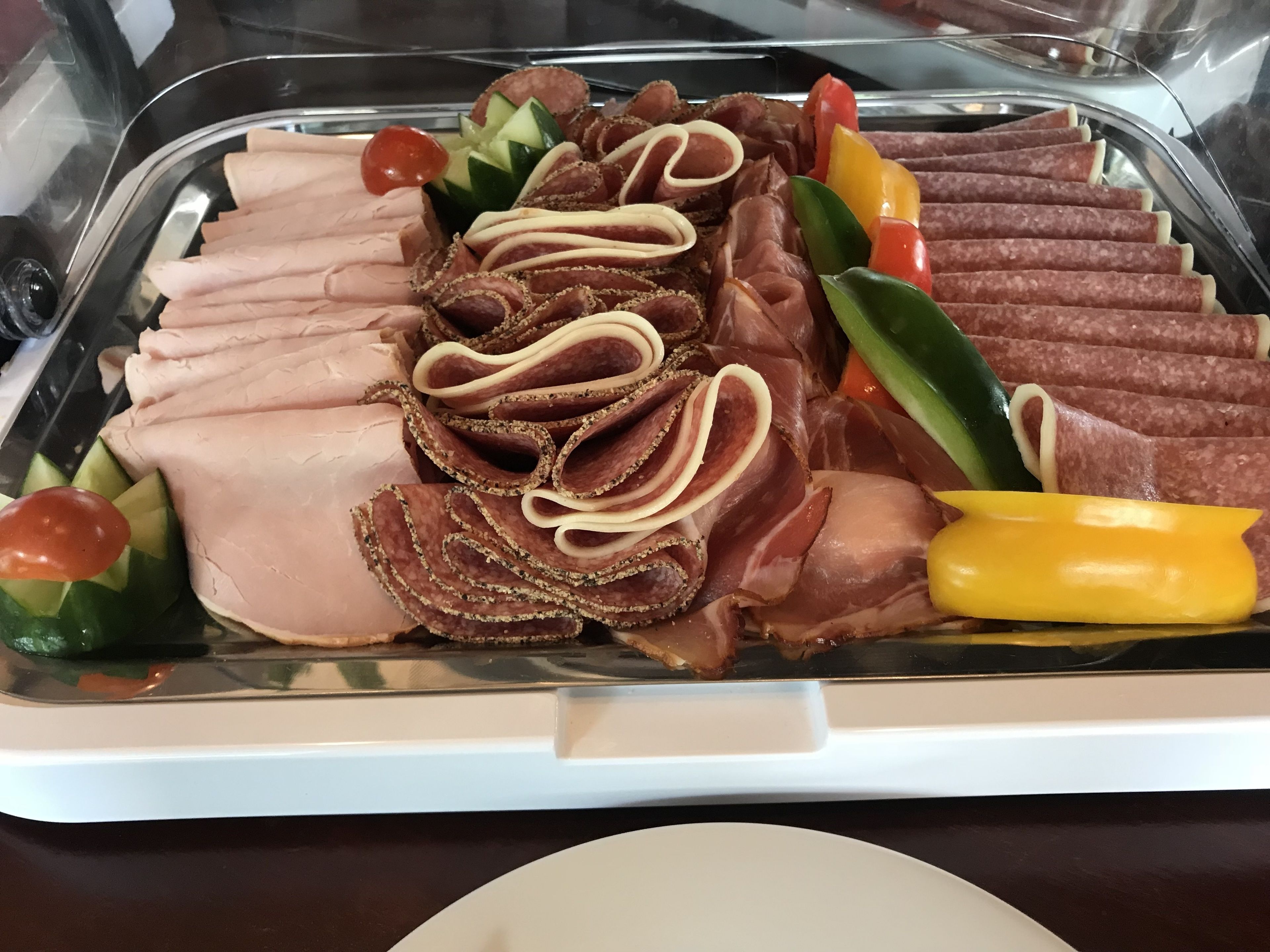 A buffet with various meats, vegetables, and a yellow condiment container.