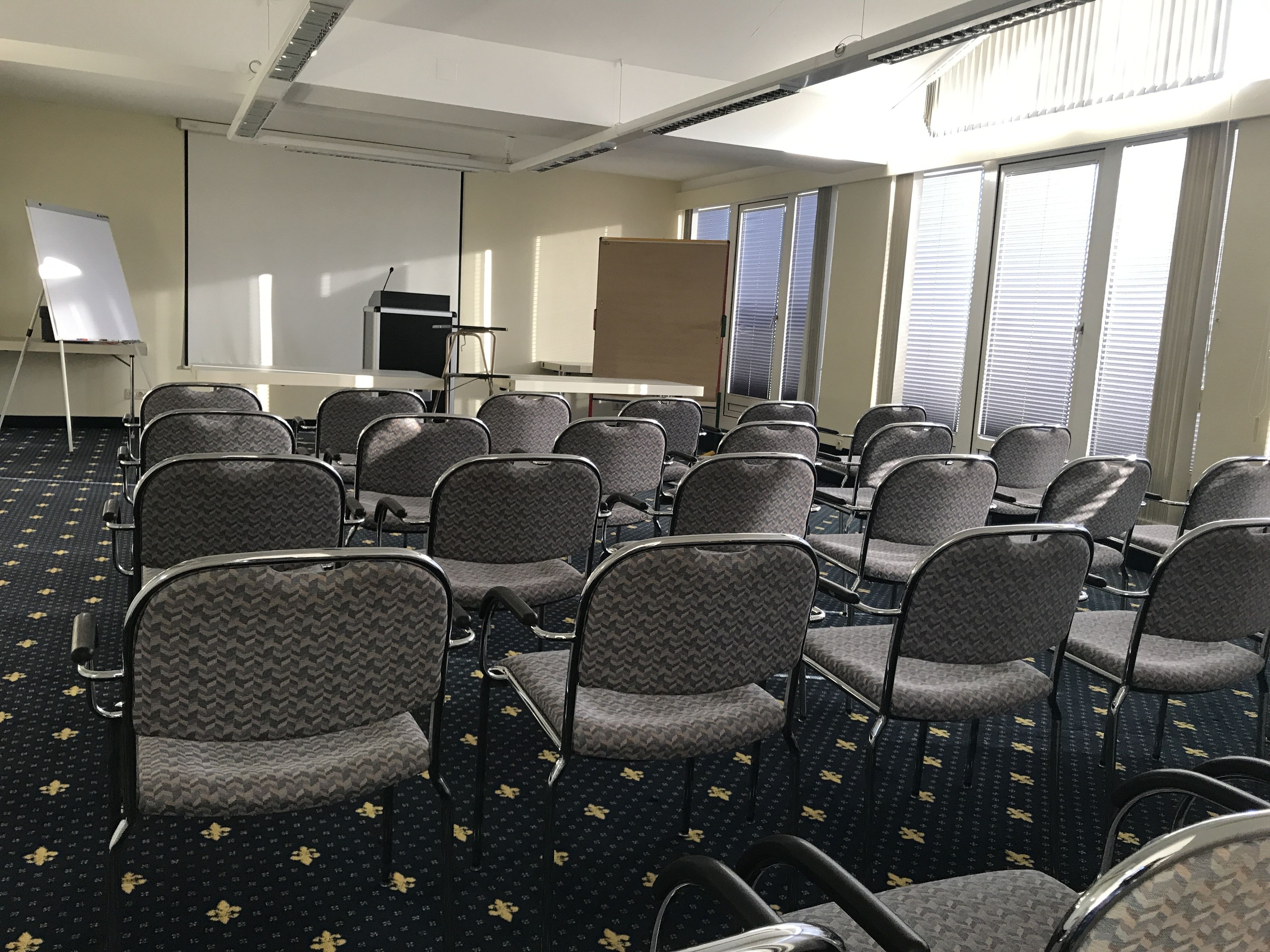 Een vergaderzaal met rijen stoelen, een whiteboard en een spreekgestalte.