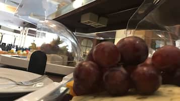 A buffet area with a glass dome covering food items, including a pile of grapes and a plate with a fork.