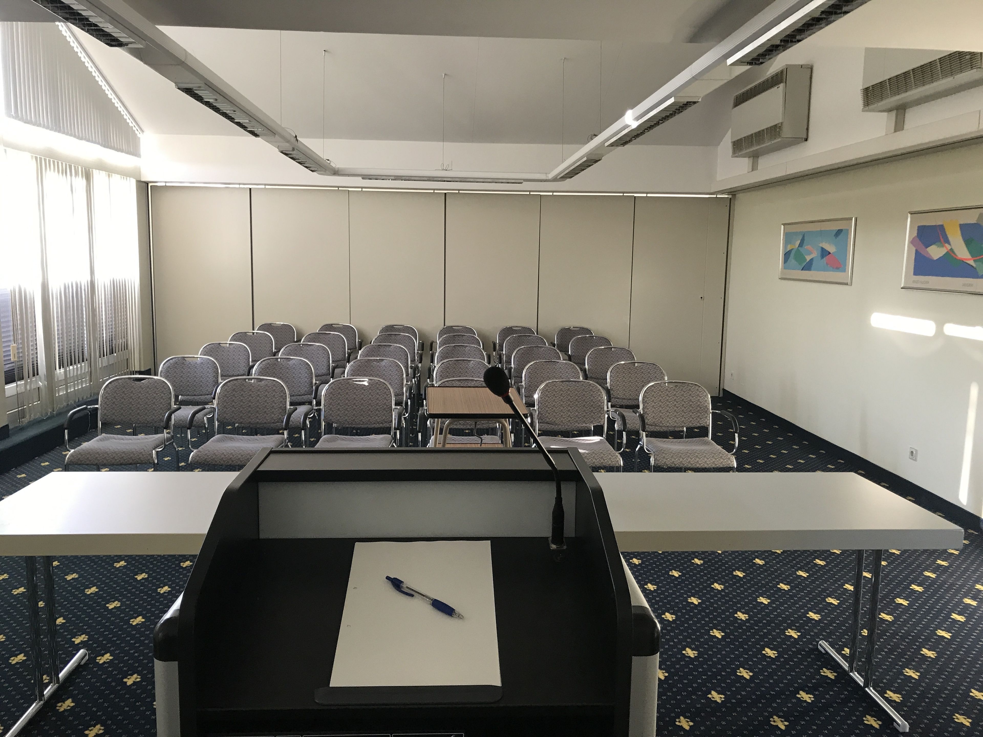 Un salón de conferencias con hileras de sillas, un atril y una pantalla de proyector.