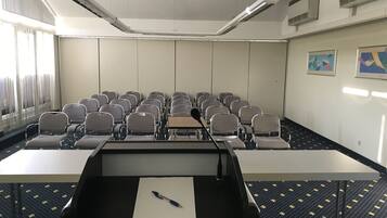 Un salón de conferencias con hileras de sillas, un atril y una pantalla de proyector.