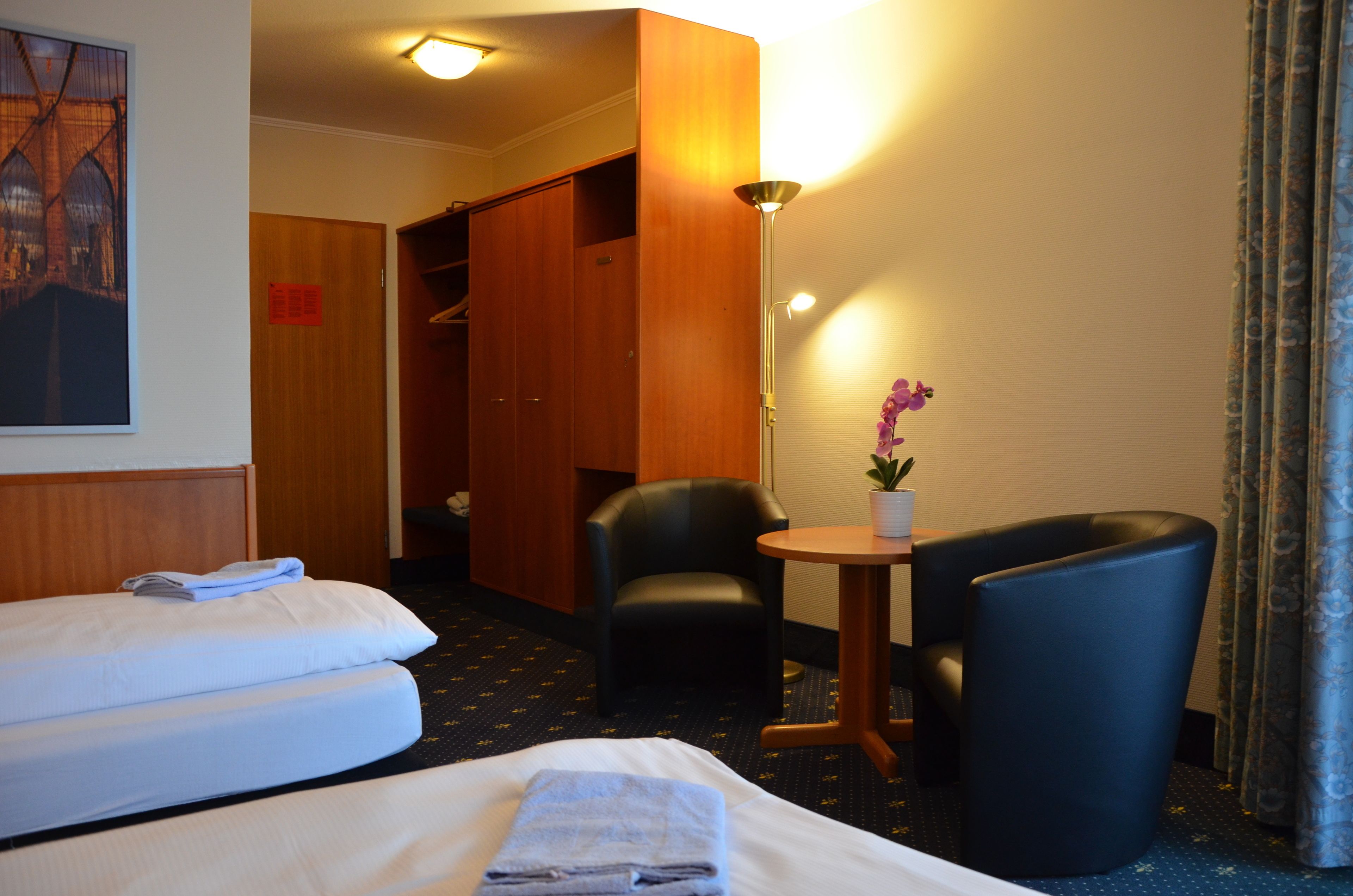 A hotel room with a bed, two chairs, a small table with a potted plant, and a wardrobe.