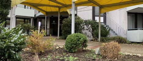 A building with a covered outdoor area featuring yellow canopies, a stone staircase, and a small garden with various plants.