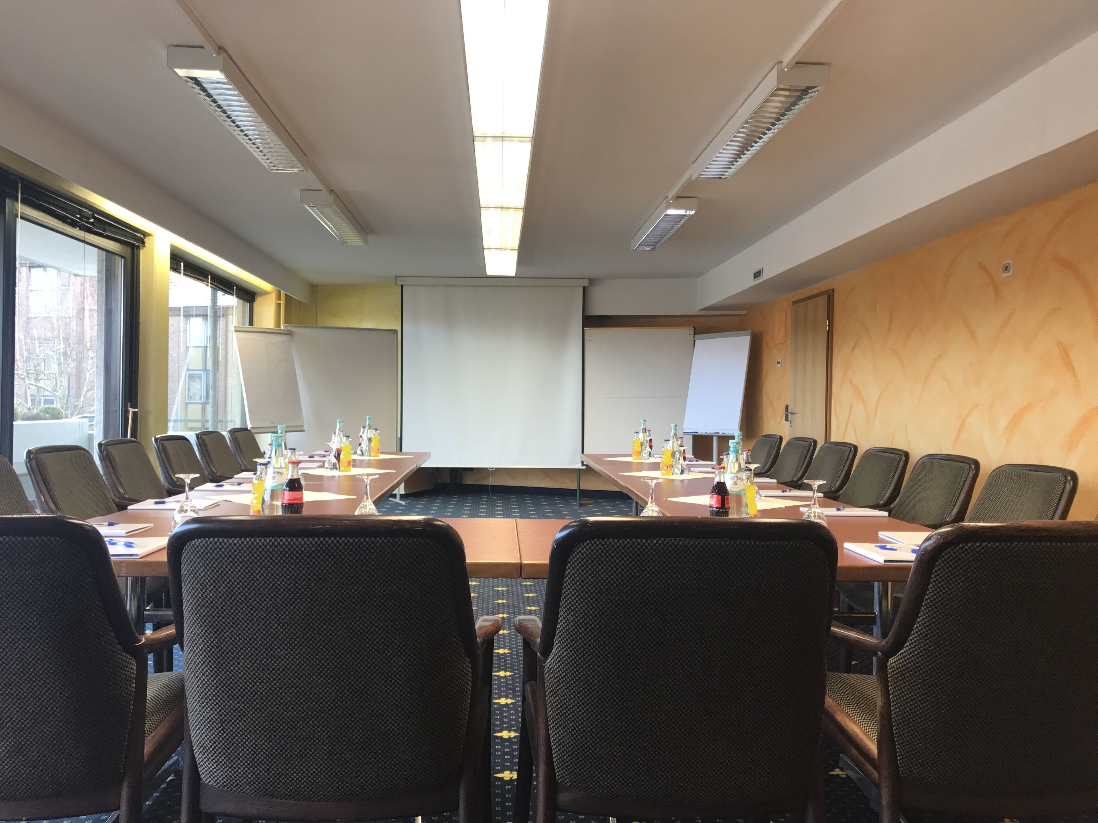 A conference room with a long table, multiple chairs, a projector screen, and a whiteboard.