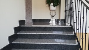 Una scala con gradini in granito e ringhiera in metallo, che porta a un pianerottolo con una pianta in vaso.
