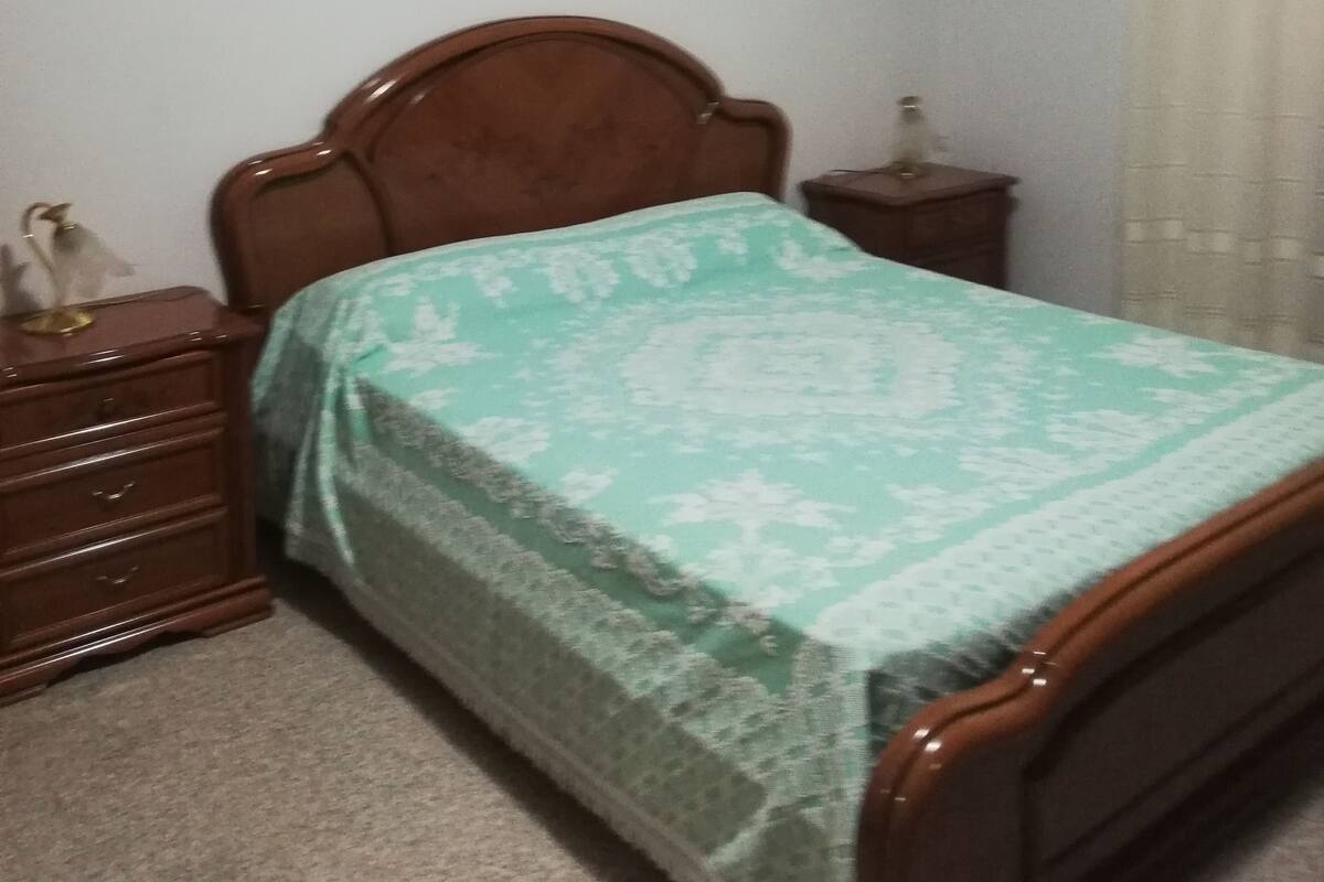 Ein Schlafzimmer mit einem hölzernen Bett, einem Nachttisch, einer Kommode und einem gerahmten Bild an der Wand.
