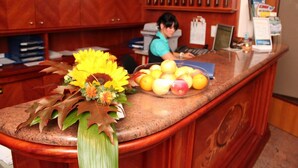Una recepción con un jarrón de girasoles, un cuenco de manzanas y un ordenador portátil.
