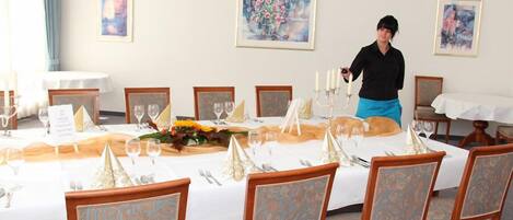 A dining room with a long table set for a meal, surrounded by chairs with patterned upholstery.