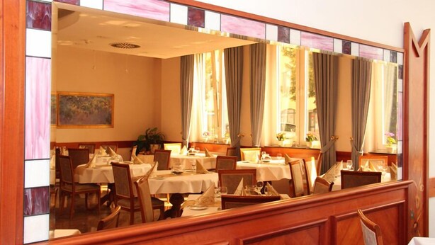 A dining area with multiple tables and chairs, a large mirror, and a painting on the wall. - Hotel Ascania (Aschersleben)