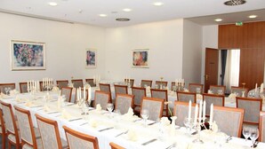 Un salón de conferencias con largas mesas dispuestas para un evento formal, con manteles blancos, velas y centros de mesa florales.