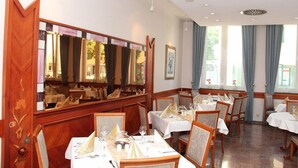 Un restaurante con varias mesas y sillas, ventanas amplias con cortinas, y un espejo que refleja el interior.