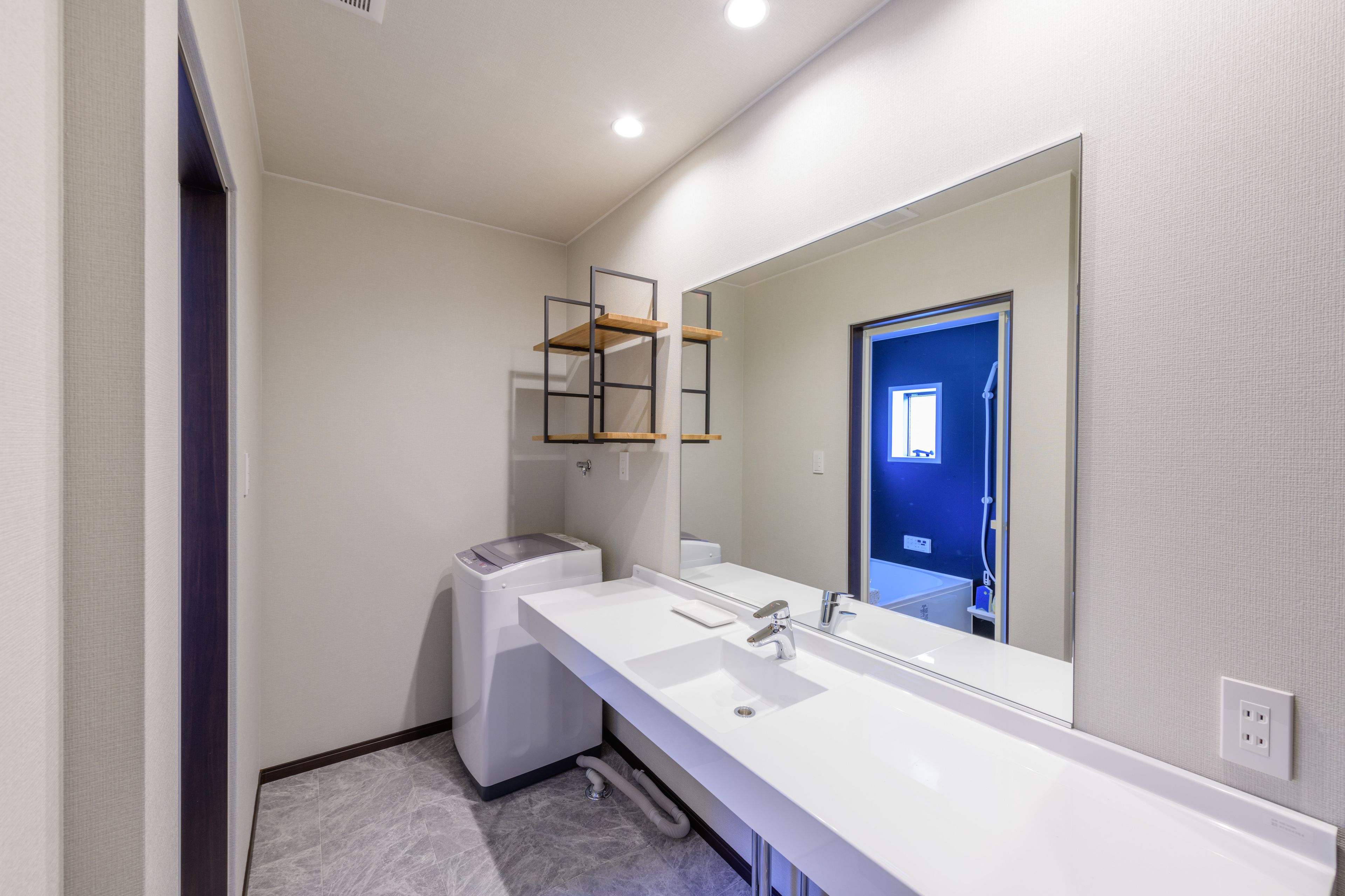 A modern bathroom with a white sink, a large mirror, and a built-in shelf.
