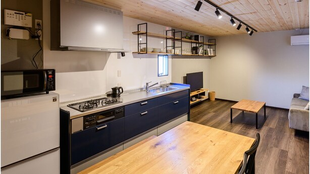 A modern kitchen with a built-in stove, microwave, and oven, a wooden dining table, and a TV in a corner. - Rakuten STAY HOUSE x WILLSTYLE SASEBO (Sasebo)