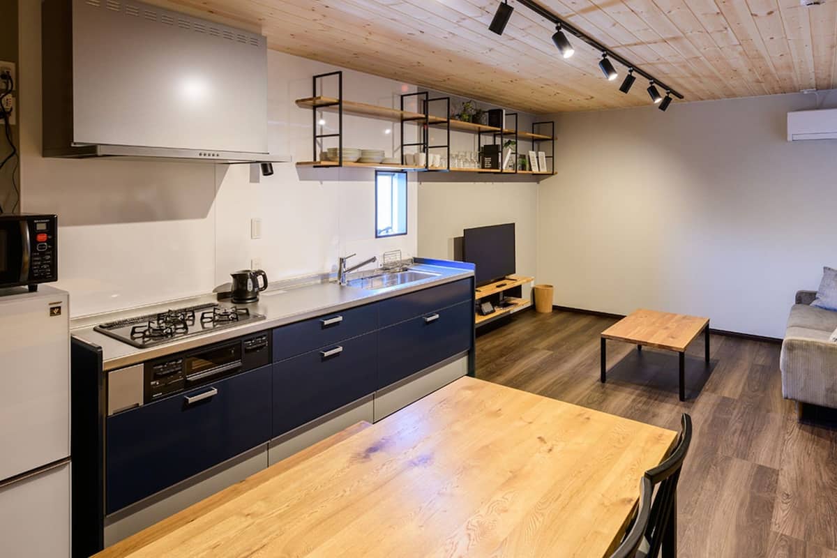 A modern kitchen with a built-in stove, microwave, and oven, a wooden dining table, and a TV in a corner.