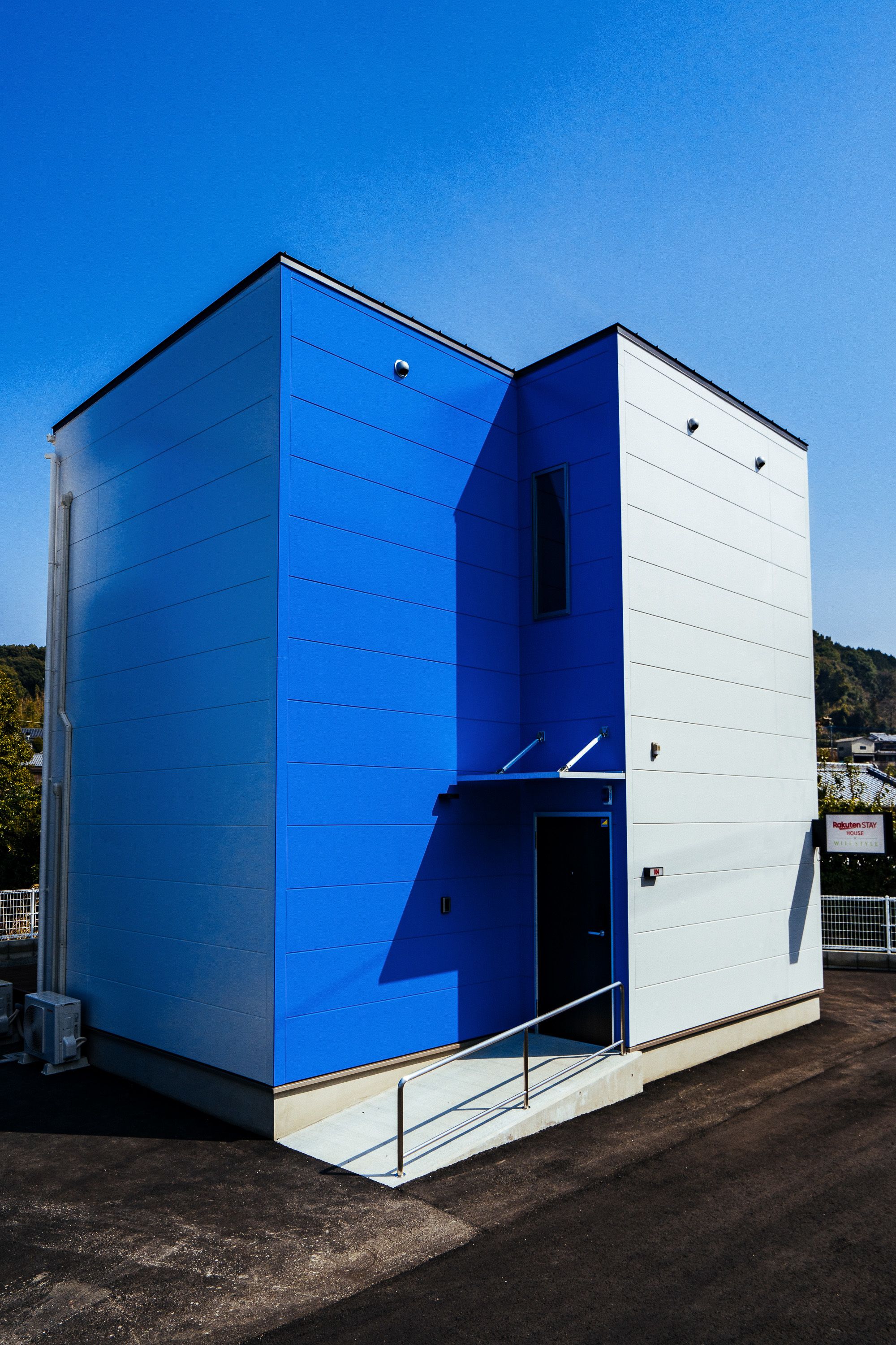 Un bâtiment moderne à la façade bleue et blanche, doté d’une entrée bien visible et d’une petite fenêtre.