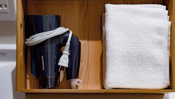 A wooden drawer containing a Panasonic hairdryer, a white towel, and a white charging cable.
