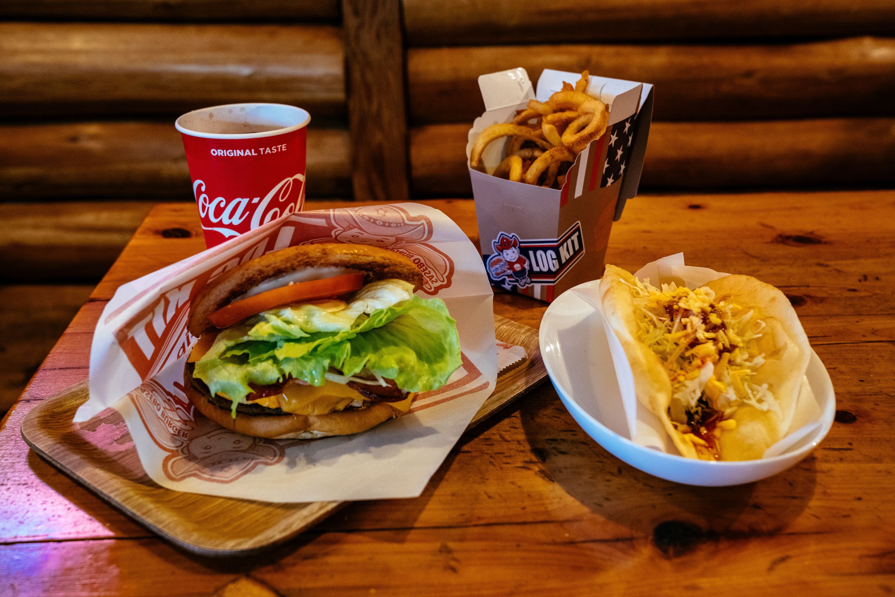 A meal consisting of a burger, a taco, and a cup of Coca-Cola on a wooden table.
