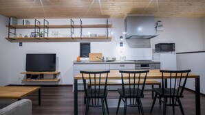 A modern kitchen with a wooden ceiling, built-in shelves, a central island with chairs, and a flat-screen TV. - Rakuten STAY HOUSE x WILLSTYLE SASEBO (Sasebo)