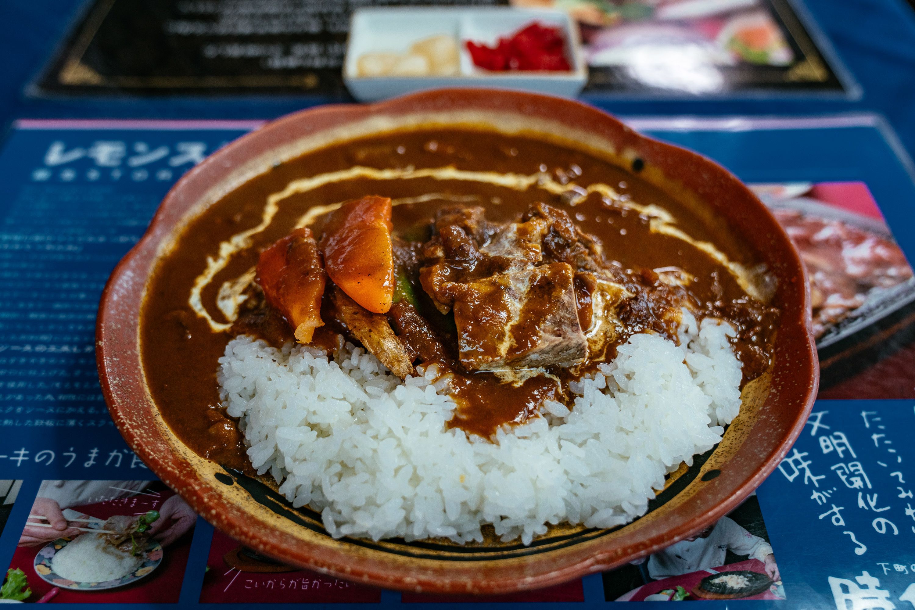 A bowl of curry with meat and rice on a table with a menu.