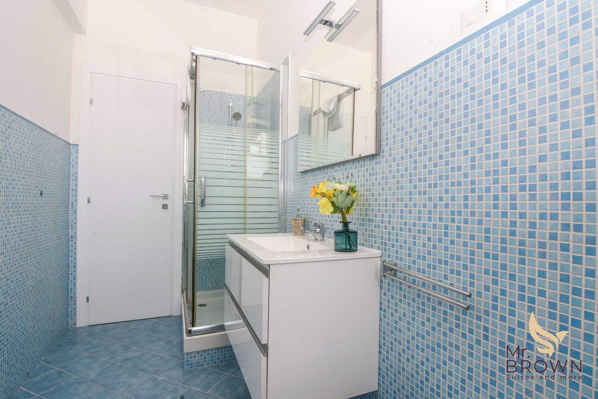 A bathroom with a white sink, a glass shower enclosure, and blue-tiled walls.