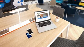 Um laptop sobre uma mesa de madeira, com um smartphone e um cabo de carregamento.