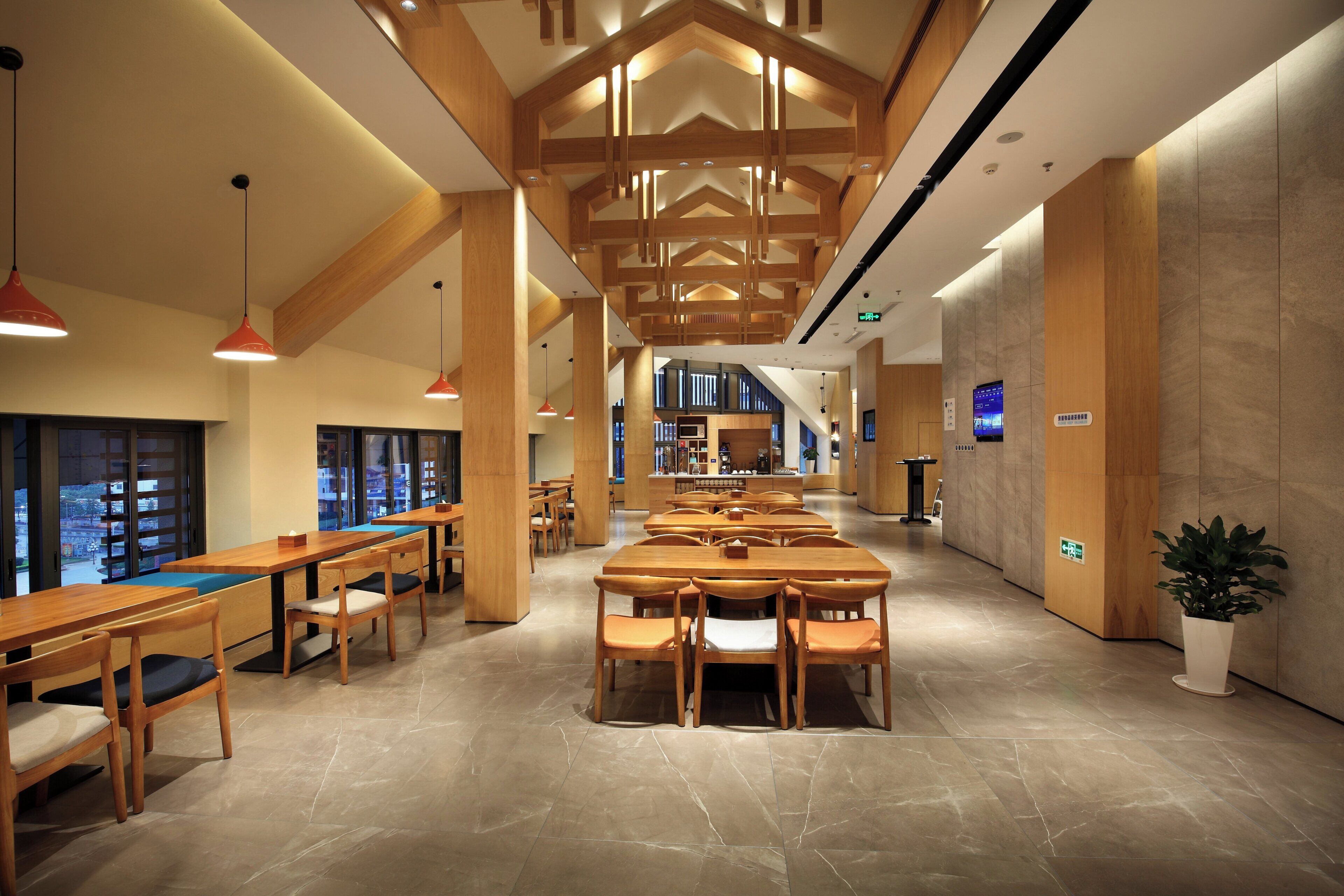 A modern interior with wooden tables and chairs, a long corridor, and a reception area with a digital display.