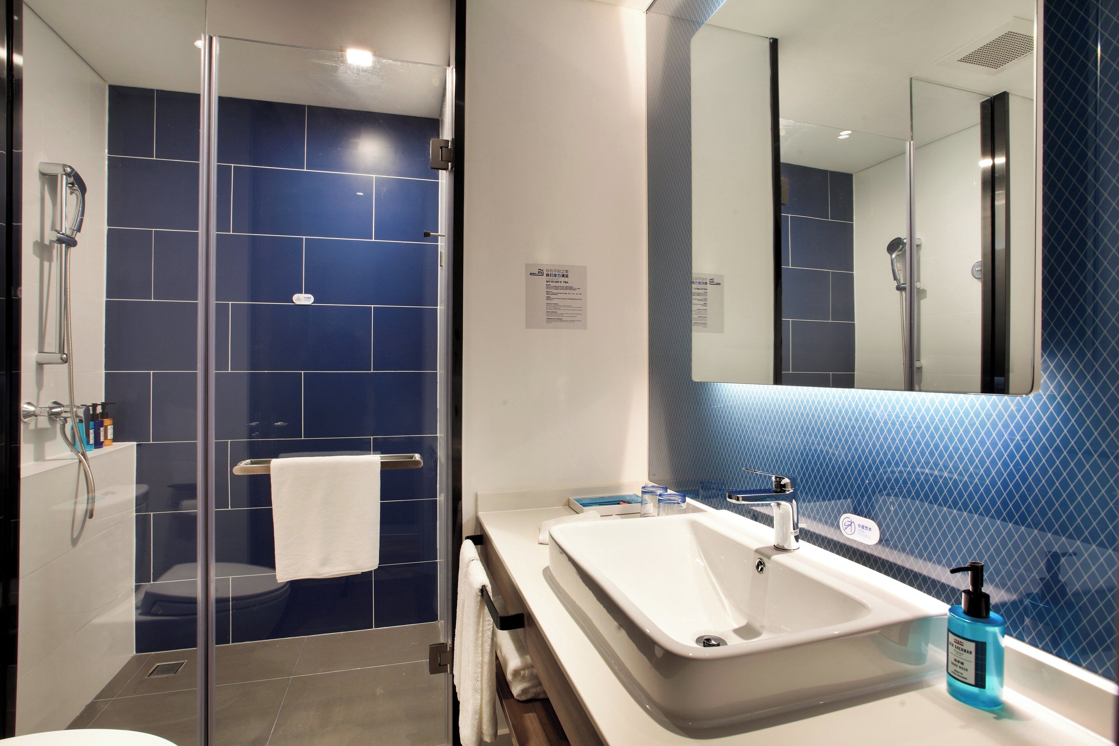 Une salle de bain moderne avec une douche à parois de verre, un lavabo blanc et un grand miroir.