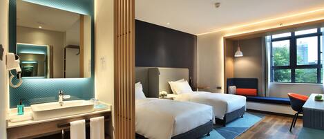 A modern hotel room with a large mirror, two beds, a bathroom with a sink and towel rack, and a view of the outdoors through a window.