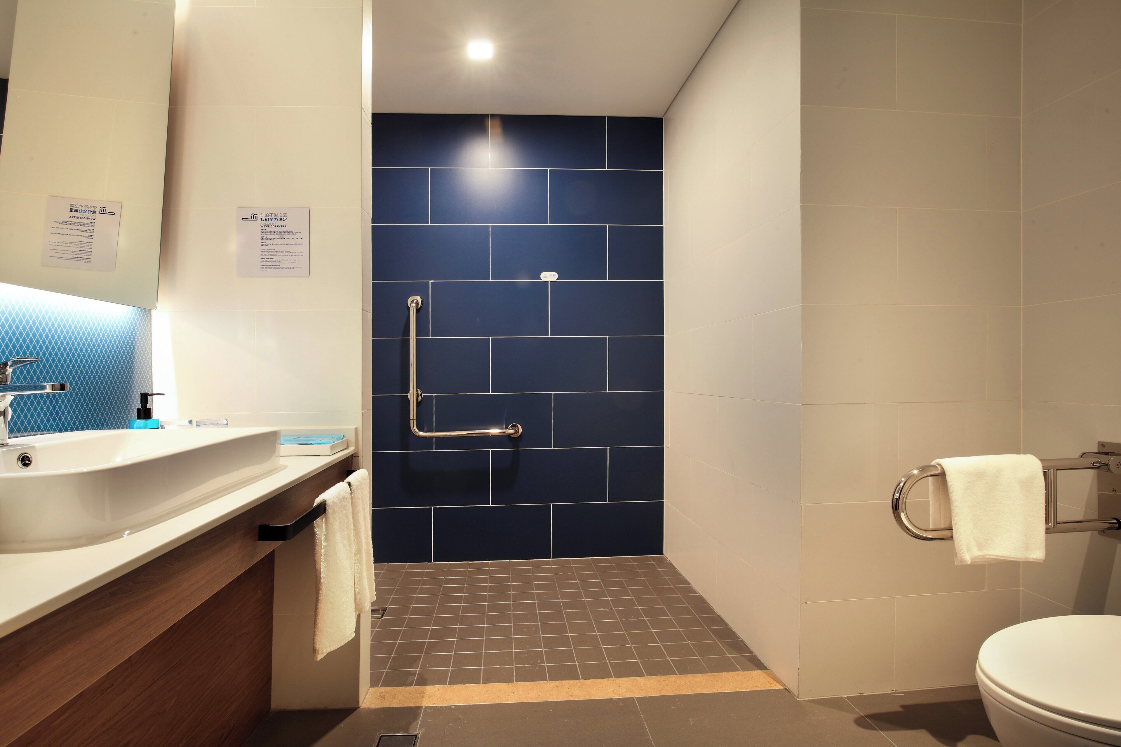 Ein Badezimmer mit weißem Waschbecken, einem Spiegel, einem Handtuchhalter und einer Toilette.