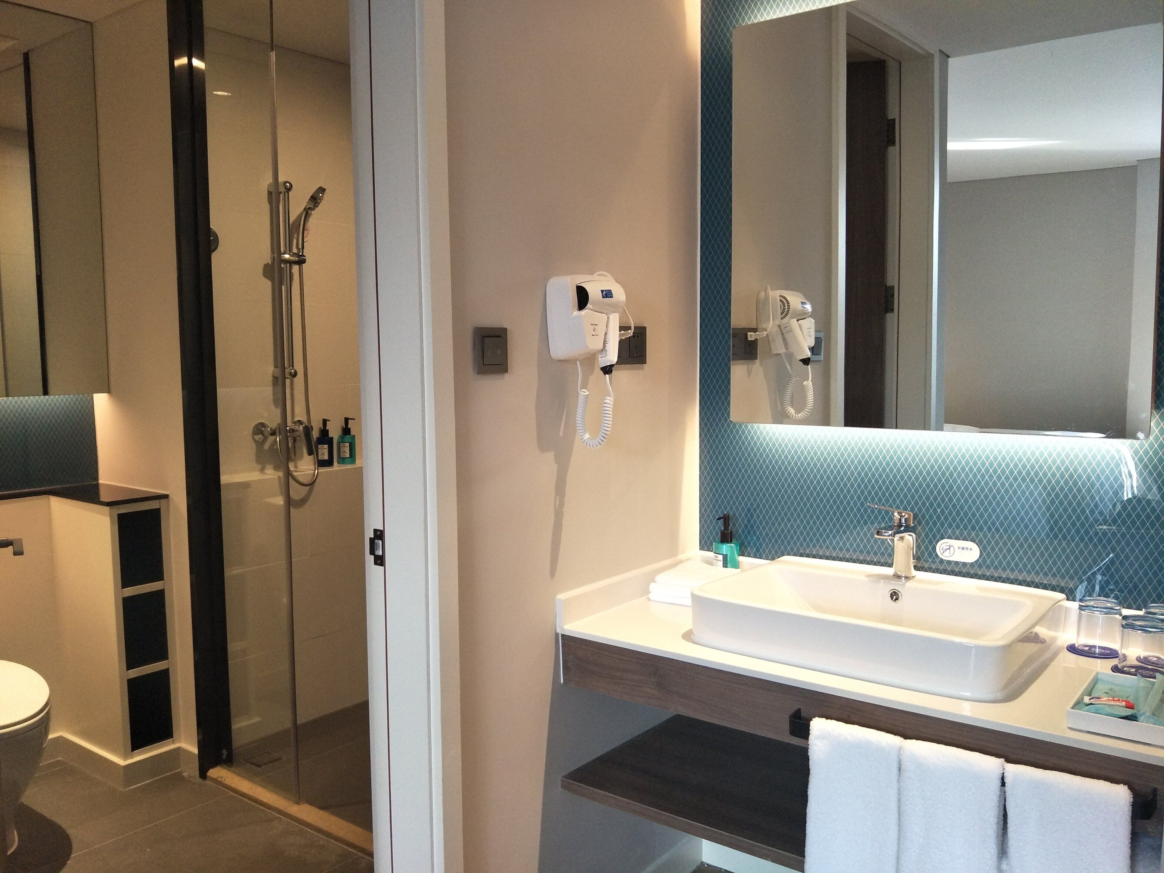 Ein modernes Badezimmer mit einer in Glas abgeschlossenen Dusche, einem weißen Waschbecken und einem großen Spiegel.