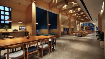 A spacious indoor area with a long wooden table and chairs, a large window, and a high ceiling with wooden beams.