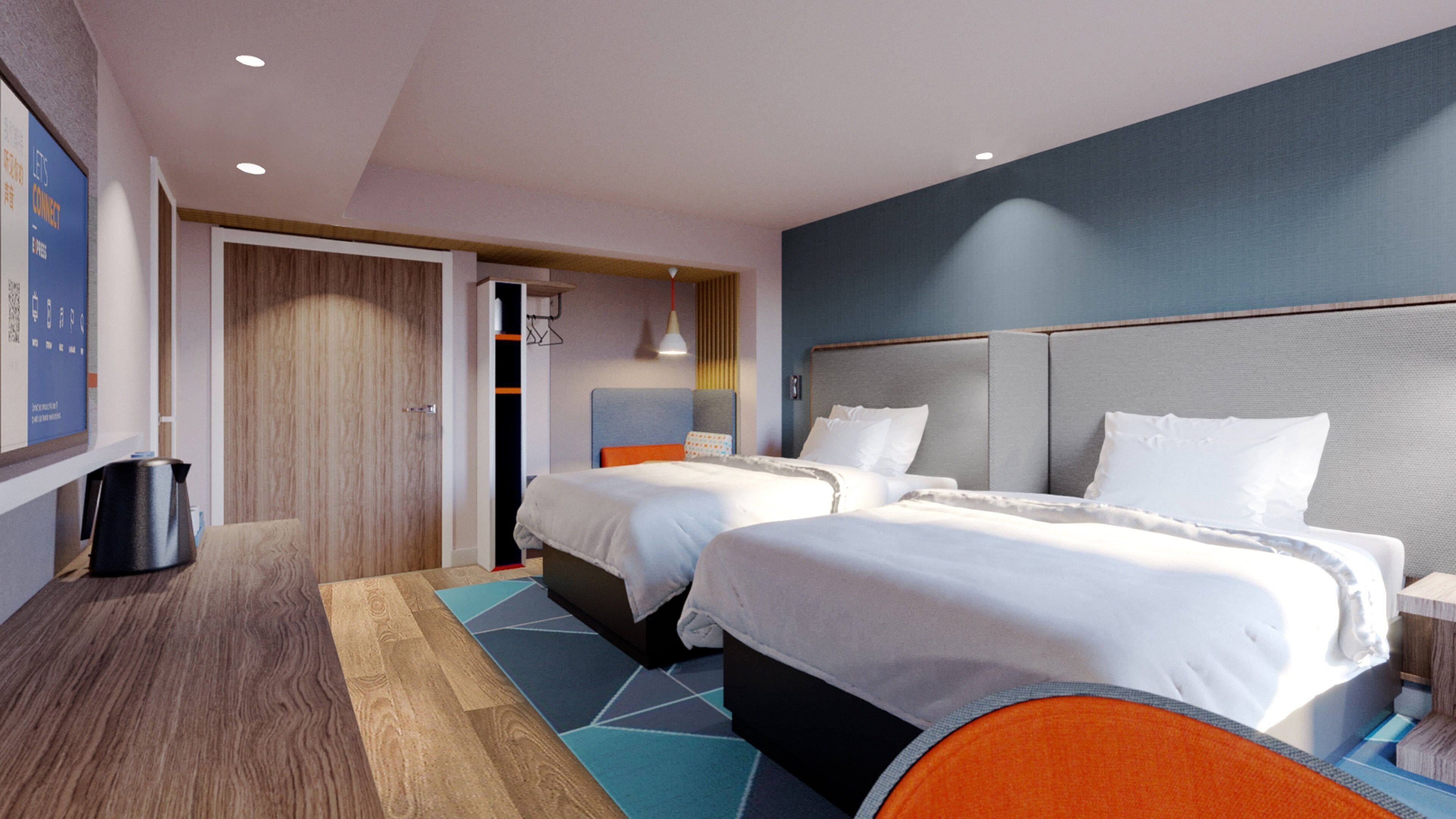 A hotel room with two beds, a wooden floor, a blue and orange rug, and a wall-mounted TV.