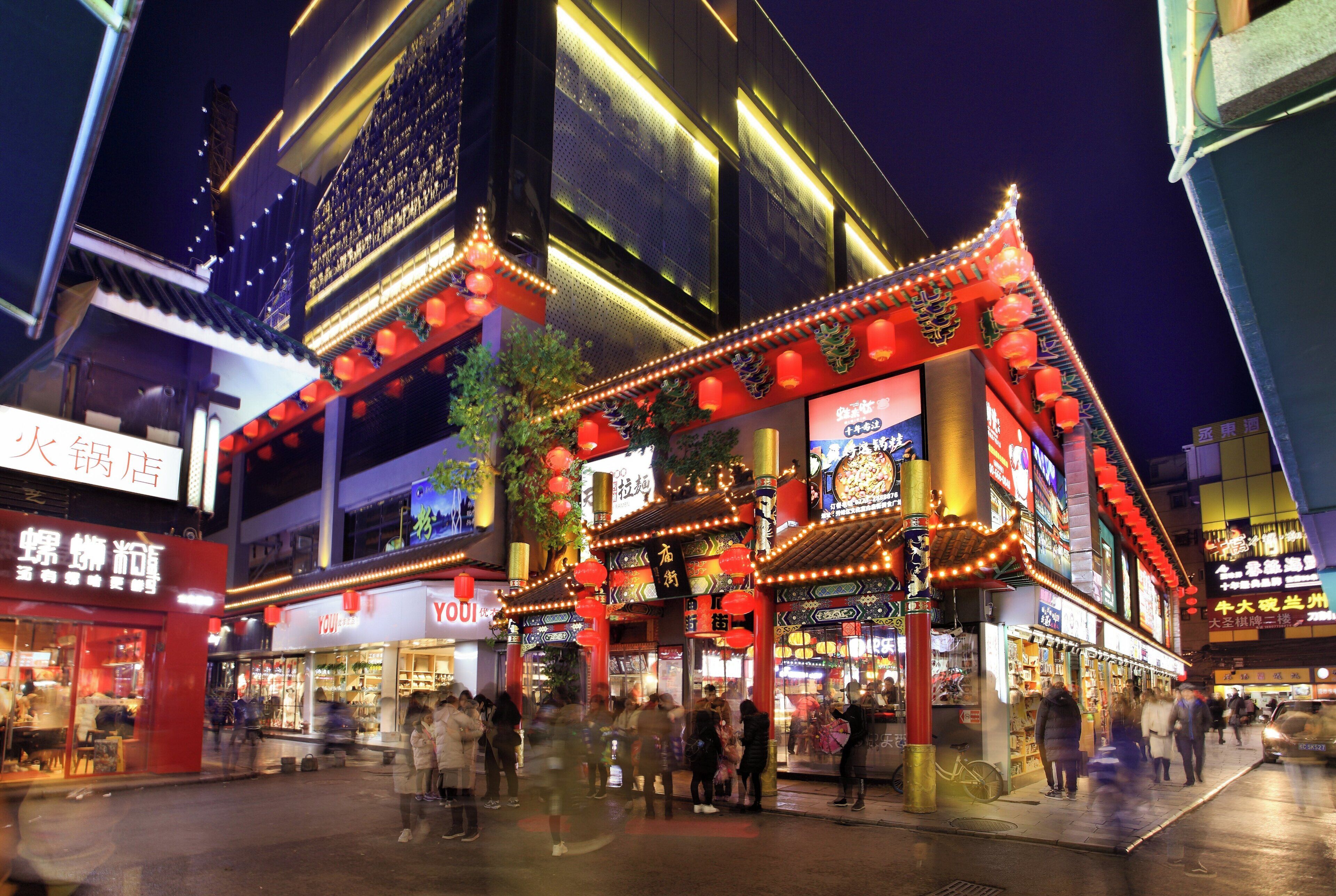 A traditional building with multiple stories, adorned with red lanterns and illuminated signage, surrounded by a bustling street scene.