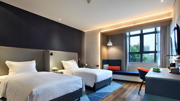 A hotel room with two beds, a desk with a chair, a large window, and a view of greenery outside. - Holiday Inn Express Guilin City Center by IHG (Guilin)