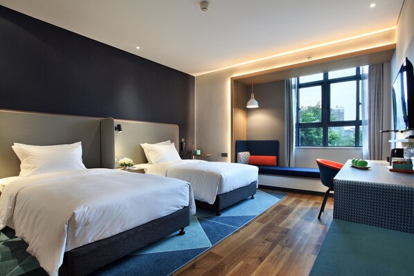 Quarto de hotel com duas camas, uma escrivaninha com cadeira, uma janela grande e vista para o verde lá fora.