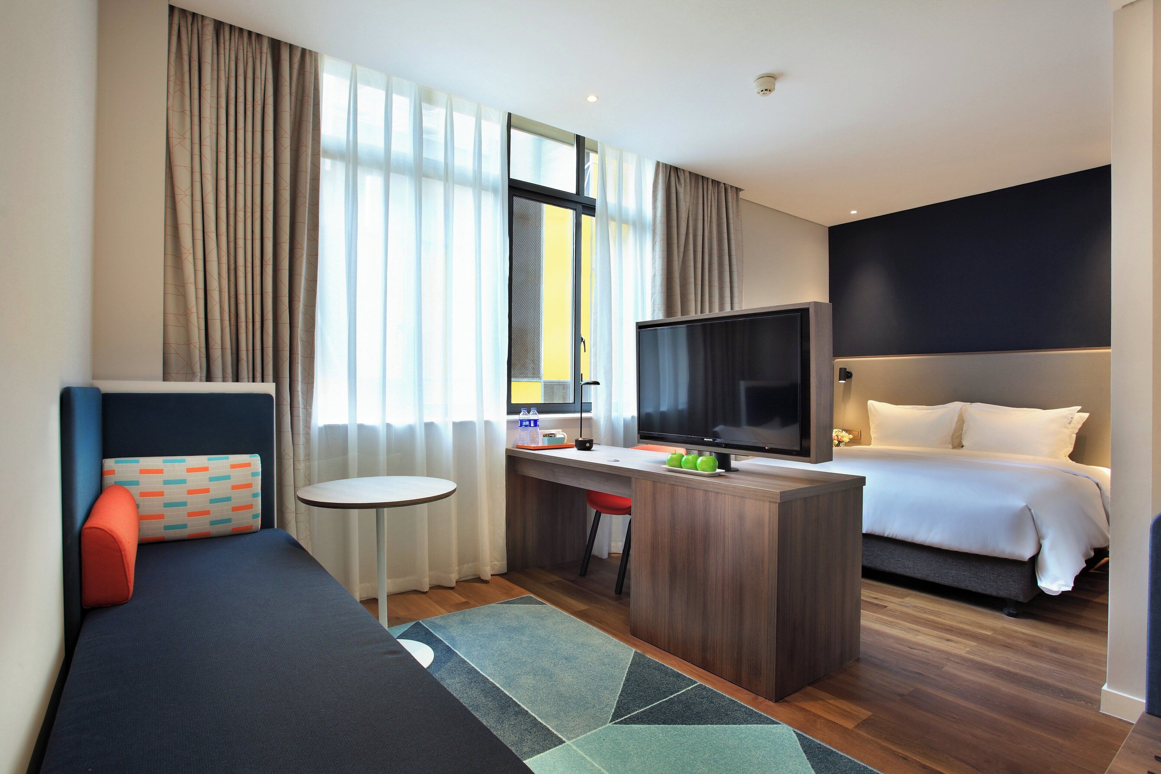 A hotel room with a bed, a desk with a TV, a sofa, and a small table.