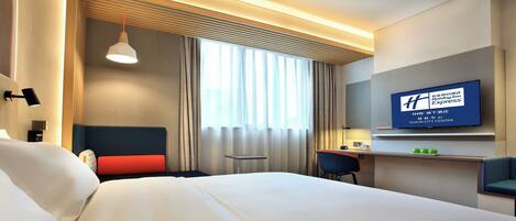 A hotel room with a bed, a desk, a chair, a TV, and a window with curtains.