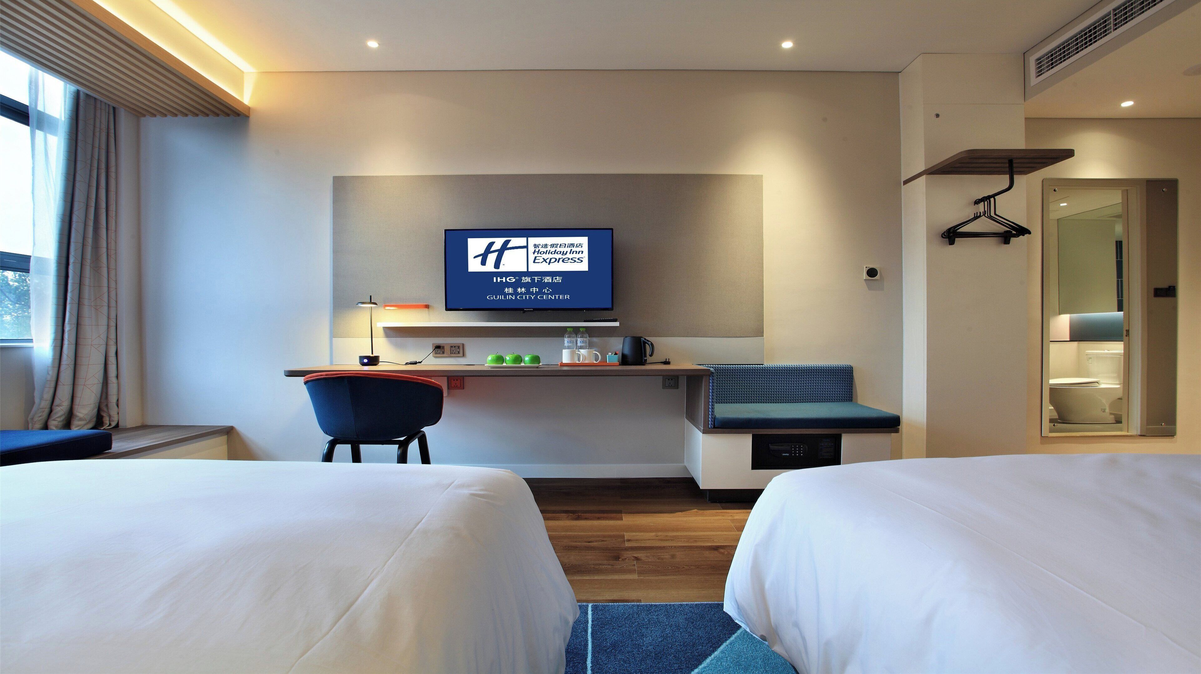 A hotel room with two beds, a desk with a computer, a TV, and a seating area.