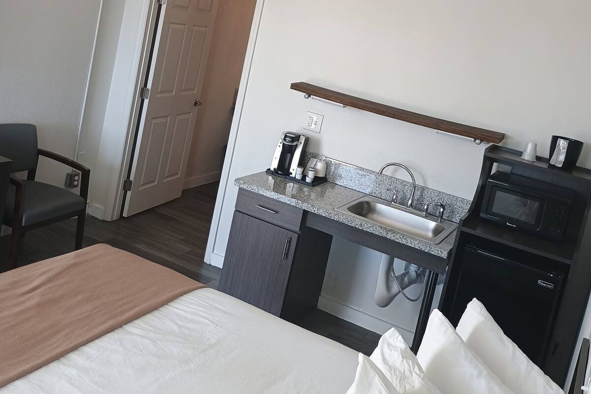 A hotel room with a bed, a desk with a coffee maker, a microwave, and a sink.