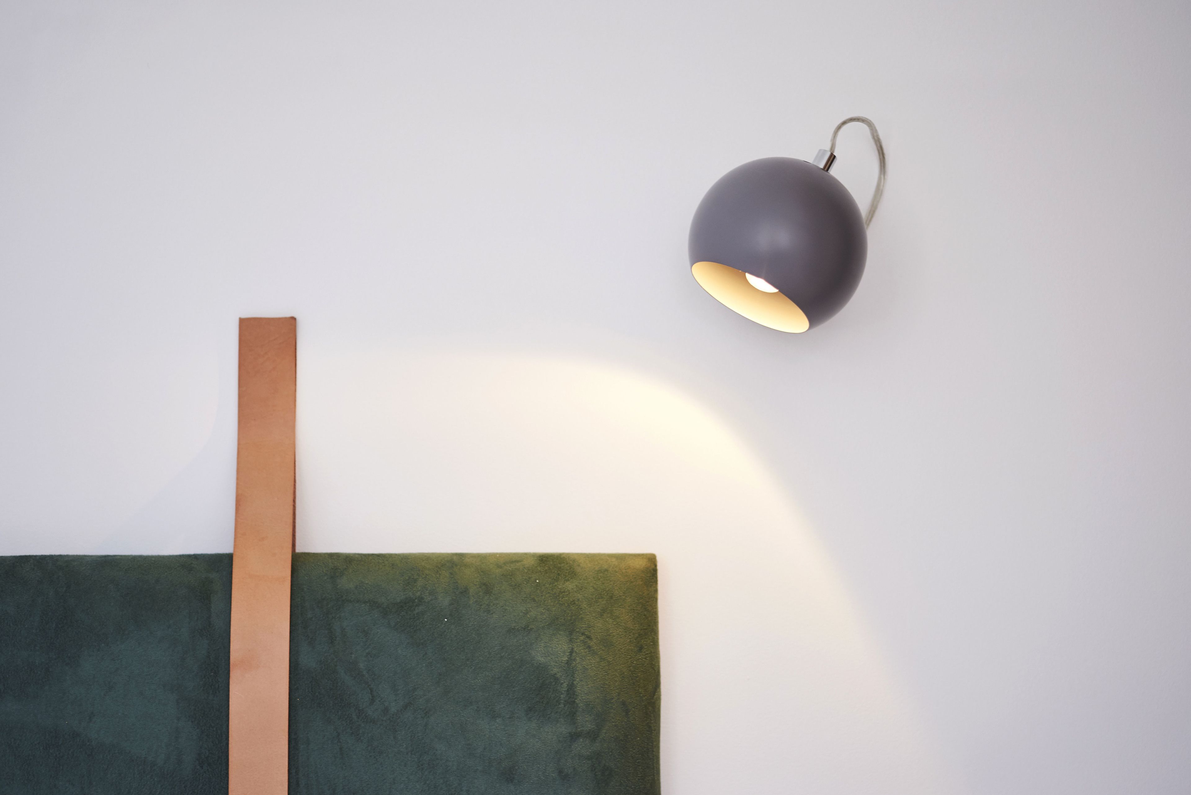 A wall-mounted lamp with a grey shade and a copper-colored object against a white wall.