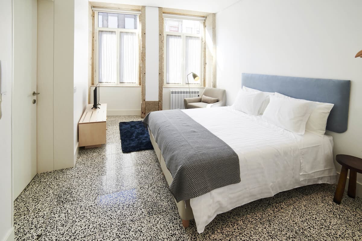 A bedroom with a bed, a chair, a desk, and a radiator.
