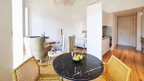 Een moderne woonkamer met een ronde zwarte marmeren tafel, rieten stoelen, een bank en een eettafel met een schaal fruit.