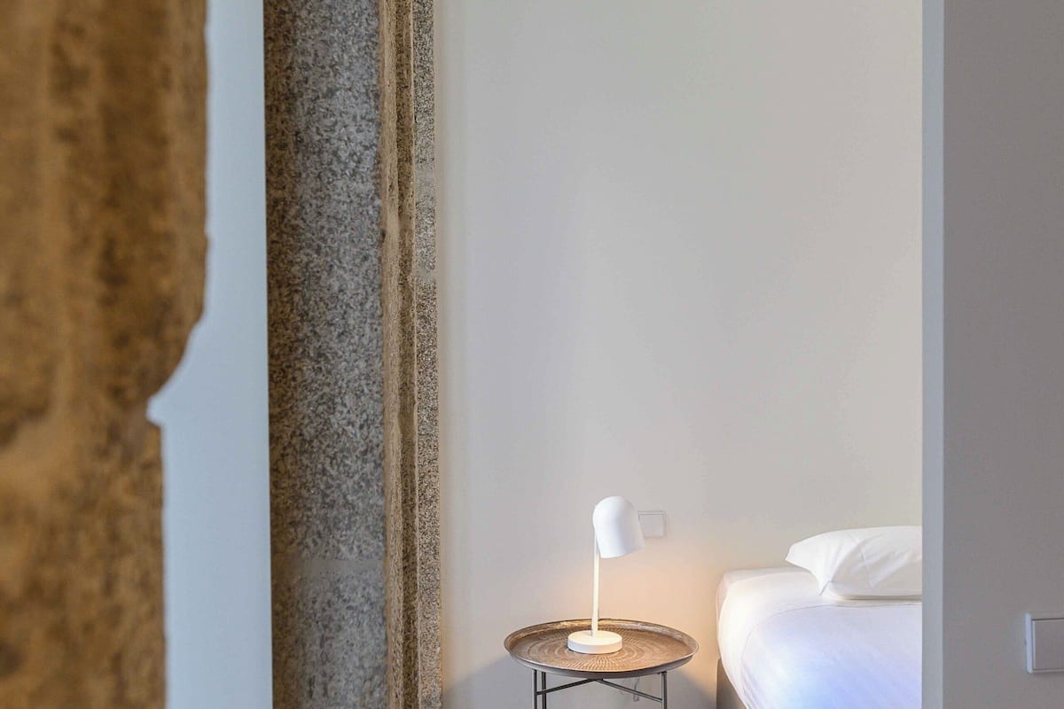 A bedroom with a bed, a bedside table with a lamp, and a wooden floor.