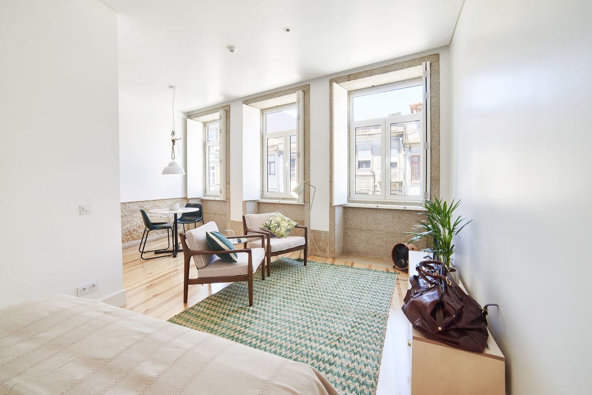 A bright room with a bed, two chairs, a table, and a large window.