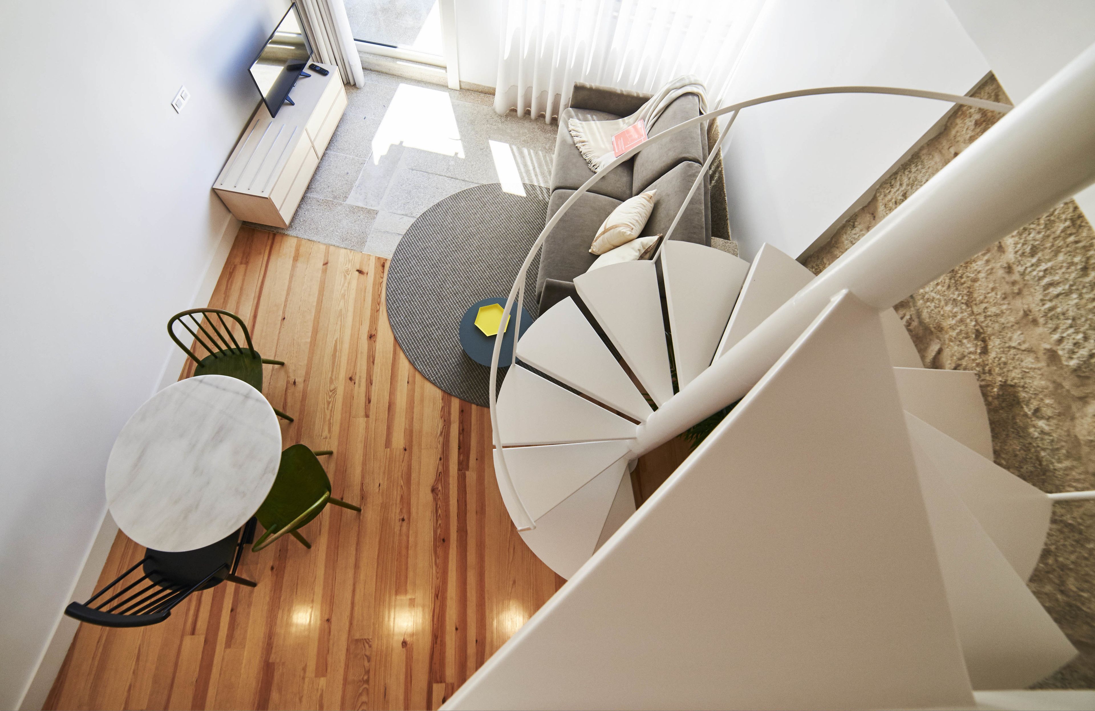 A modern interior with a spiral staircase, a round table with chairs, and a sofa with cushions.